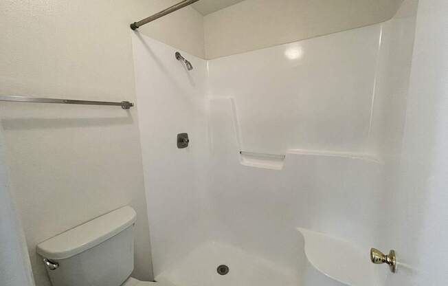 A white bathroom with a toilet, a shower, and a towel bar.