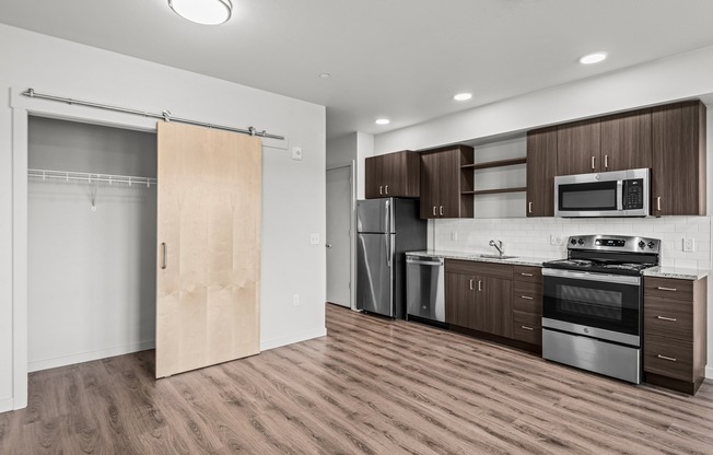 Studio kitchen with stainless-steel dishwasher, oven, range, microwave, and refrigerator, granite countertops and white subway-style backsplash featuring a barn-door style closet