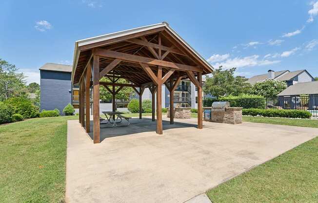 A pavilion with a wooden roof and a concrete floor is surrounded by greenery.