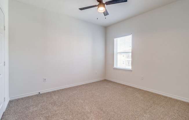 an empty bedroom with a ceiling fan and a window