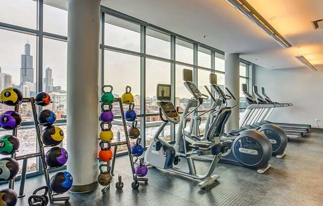 Community fitness room with cardio machines and floor-to-ceiling length windows with a city view at The Madison at Racine, Illinois