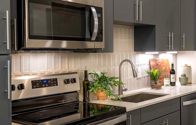 Enhance your kitchen's elegance with the Chrome Symmons faucet featuring a pull-down spray head, perfectly complemented by a stylish tile backsplash in Modera Garden Oaks.