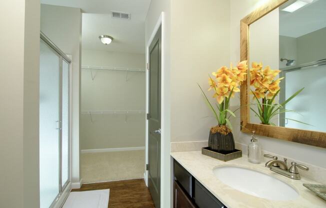 A bathroom with a sink, mirror, and a vase of flowers.