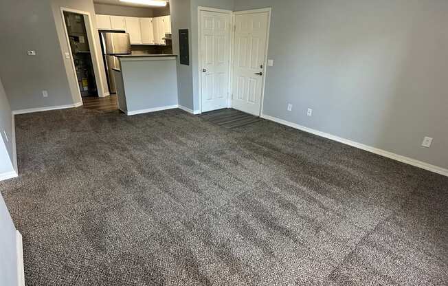 an empty living room with a ceiling fan and a kitchen in the background