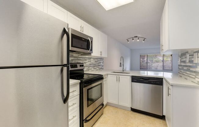 Kitchen with cabinets, sink with vegetable sprayer, tile back splash, stainless steel oven, microwave, and refrigerator, and dishwasher.