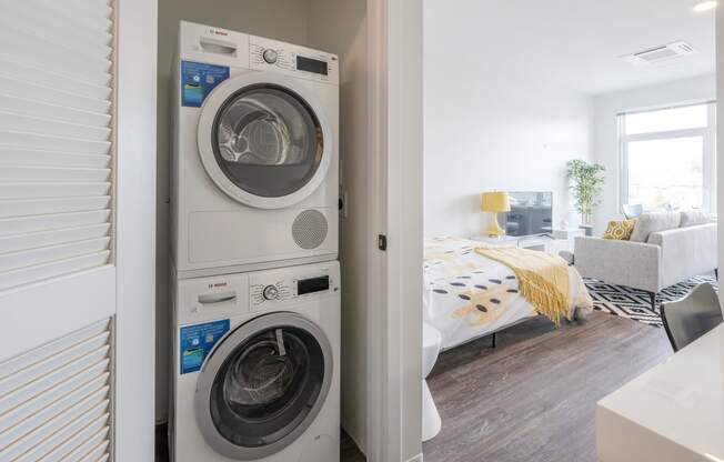 a front loading washer and dryer in a bedroom with a bed