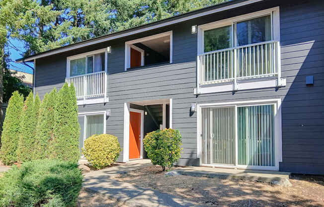 A grey two-story house with a red door and a balcony on the second floor.