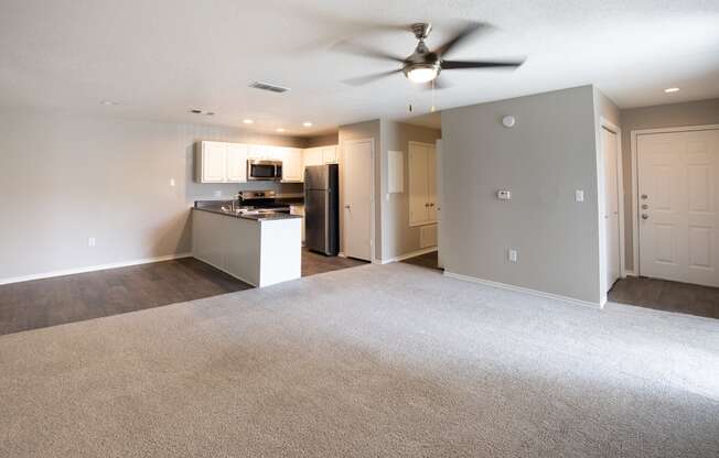 View of living area and open kitchen. Featuring carpet flooring in living area and wood look flooring in kitchen and dining room, with stainless appliances and dark counters.