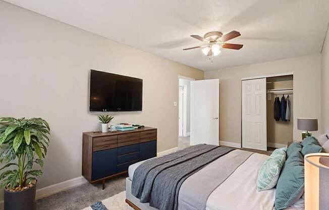 A bedroom with a bed, a dresser, a plant, and a ceiling fan.