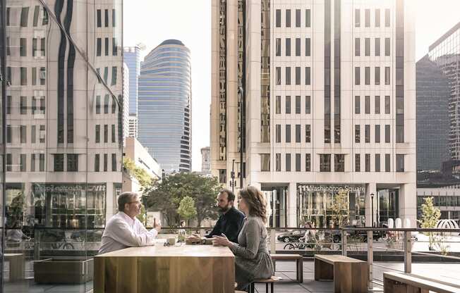 Three people are sitting at a table in a city outdoor cafe.