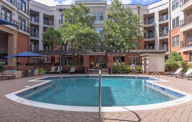 A swimming pool surrounded by a brick patio and lounge chairs.