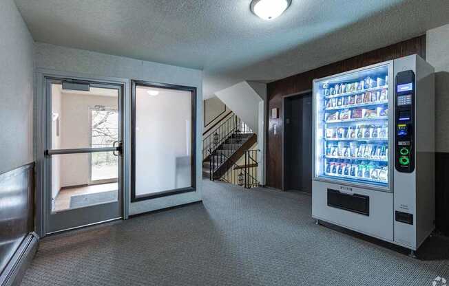 A vending machine is in a hallway with a staircase.