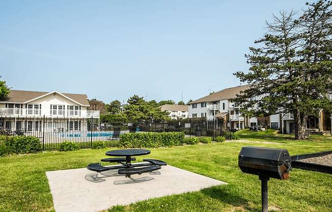 a picnic table and grill sit on a concrete slab in a grassy area with a pool