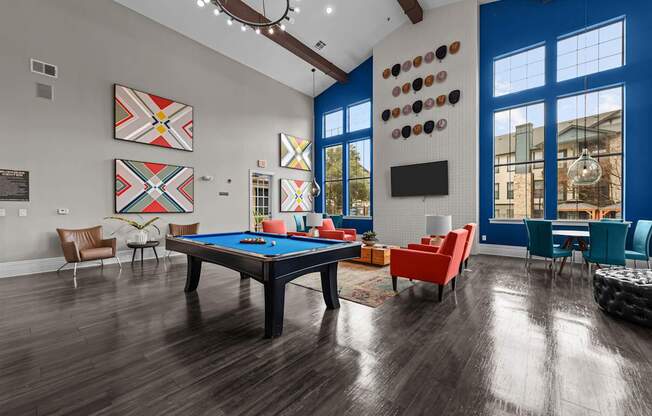A pool table is surrounded by chairs in a room with wood flooring.