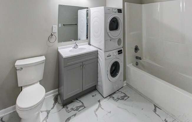 a white bathroom with a washing machine and a toilet and a sink