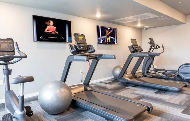 four treadmills and exercise balls in a gym with televisions on the wall