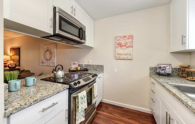 Model home kitchen with granite counter tops, white cabinets and wood flooring.  Kitchen comes with refrigerator, microwave, stove and dishwasher. at Monte Bello Apartments, Sacramento, California