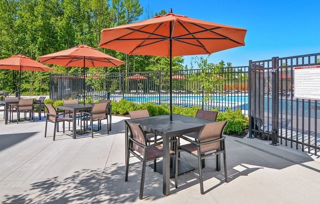 our patio has tables and chairs with umbrellas and a pool in the background