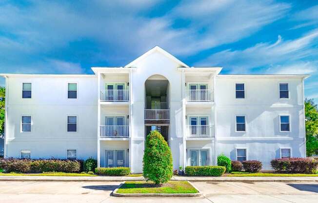 A white two-story apartment building with a balcony on the second floor.