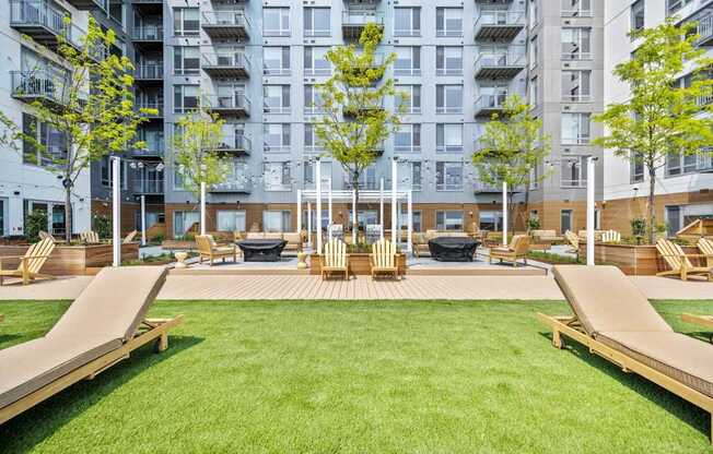 A large grassy area with wooden benches and a tree in the middle of a courtyard surrounded by buildings.