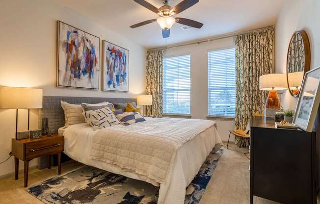A bedroom with a large bed, a ceiling fan, and two lamps.