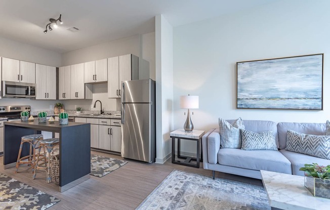 a living room with a couch and a chair in front of a kitchen with stainless steel appliances