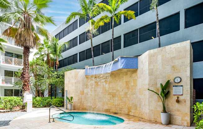 A pool surrounded by a stone wall and palm trees.