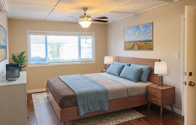 A bedroom with a bed, nightstand, and a painting on the wall.