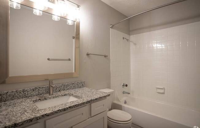 A bathroom with a granite countertop and white fixtures.