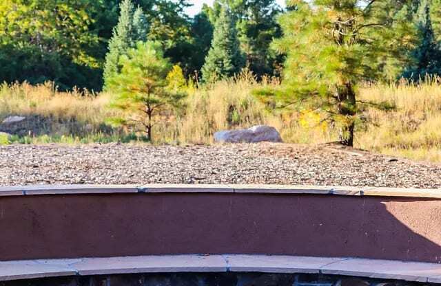 A hot tub sits in the middle of a rocky area with trees in the background.