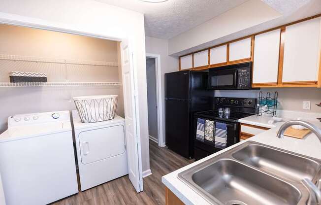 A kitchen with a white washing machine and a black refrigerator.