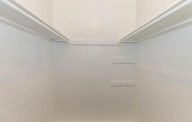 Empty closet interior with white walls and two horizontal rods for hanging clothes. The space appears clean and unadorned, with a couple of built-in shelves on the back wall. Ideal for storage or organization purposes.