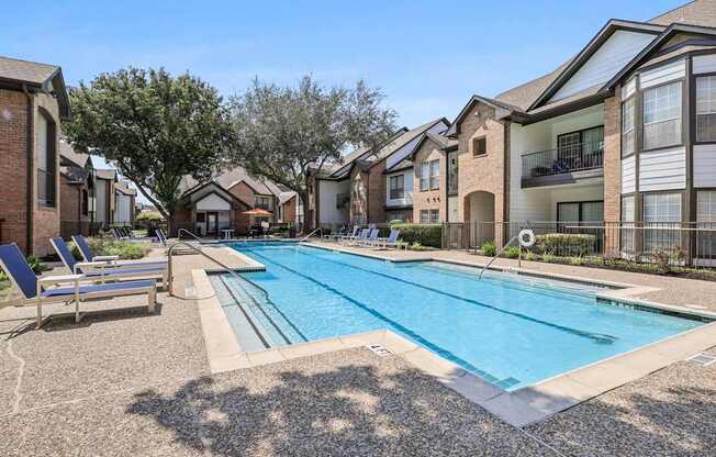 A swimming pool surrounded by apartment buildings and lounge chairs.