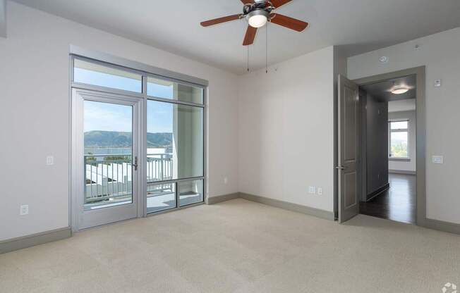 A room with a ceiling fan and a large window overlooking a balcony.