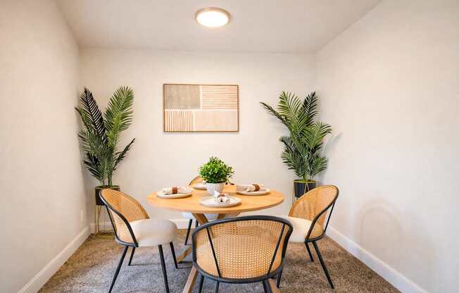 A dining room with a table set for two and a plant on each side.