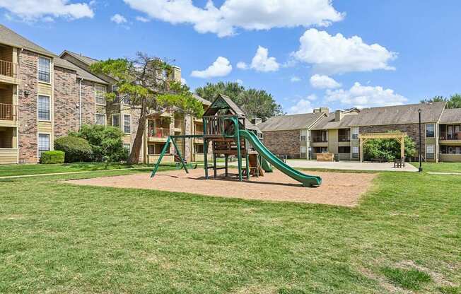 A playground with a green slide and a wooden swing set.
