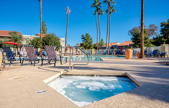 A hot tub sits in the middle of a patio with chairs and palm trees in the background.