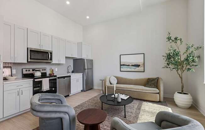 A modern living room with grey and white furniture and a kitchen area in the background.
