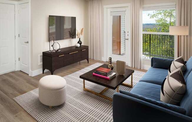 A living room with a dark blue sofa, a wooden coffee table, a white ottoman, and a flat-screen TV mounted on the wall.