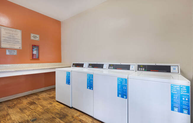 four washers and dryers in a laundry room with orange walls and wooden floors