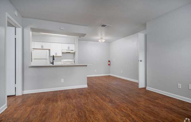 the living room and kitchen of an apartment with wood flooring and white cabinets