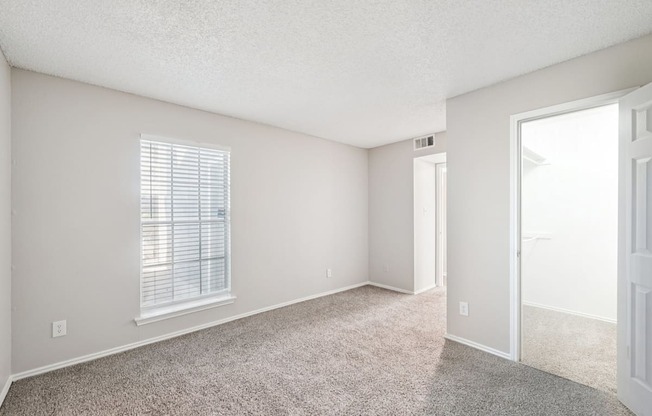 A room with a carpeted floor and a window with blinds.