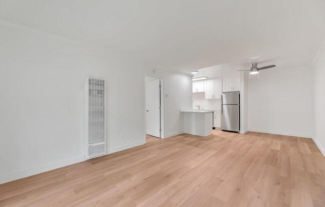 A room with wooden flooring and a kitchenette in the background.