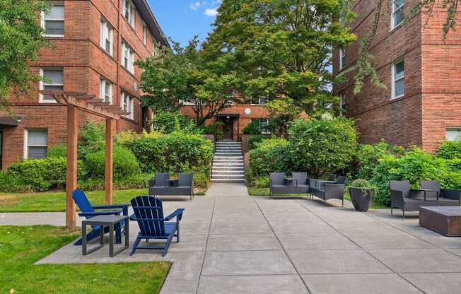 A courtyard with a concrete floor, blue chairs and tables, and a brick building in the background.