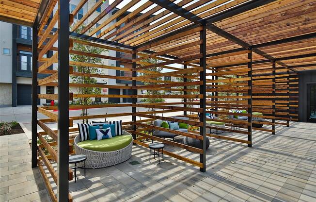 Three outdoor lounge areas with comfortable seating under a pergola structure near The Shiloh apartment buildings.