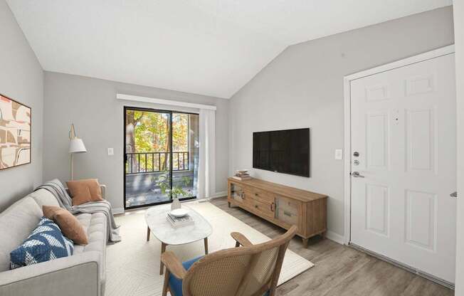 A living room with a grey couch, a white coffee table, a wooden chair, a flat screen TV, and a sliding glass door.