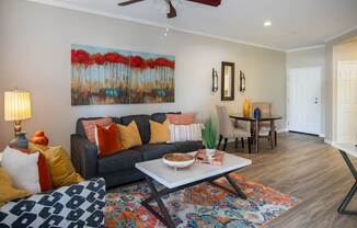 A living room with a grey couch, a painting of red flowers, and a rug with a geometric pattern.