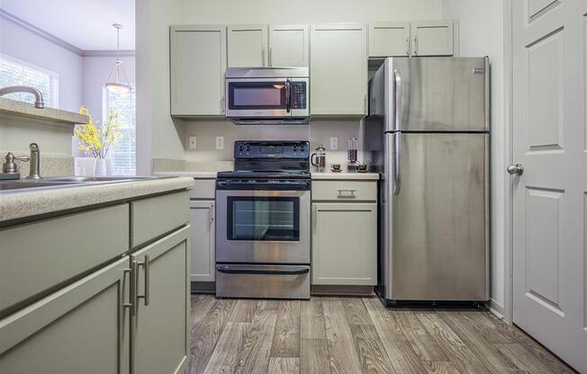 Tallahassee FL apartment kitchen area with stainless steel appliances, shaker-style cabinetry, and wood-designed flooring at Evergreens at Mahan