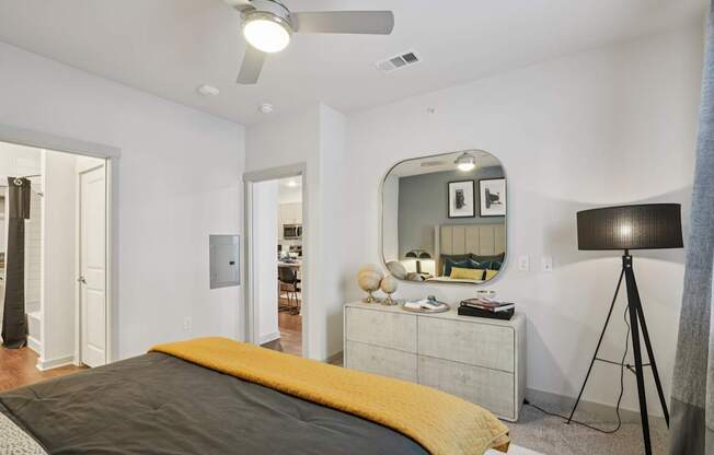 A bedroom with a bed, dresser, mirror, and a ceiling fan.