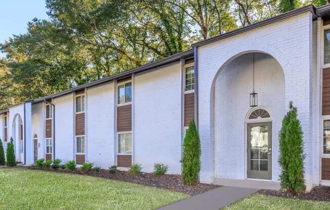 the exterior of a white brick building with a front door and a lawn